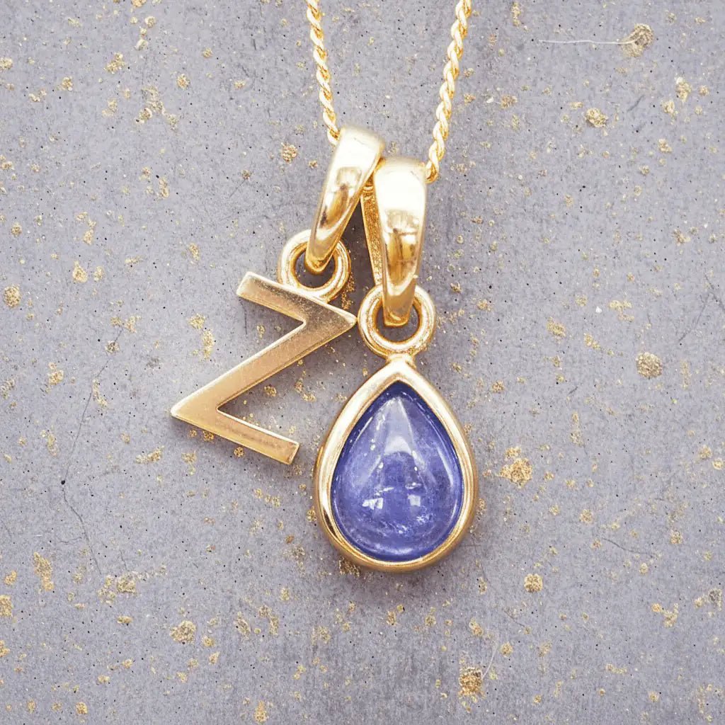 Gold December birthstone necklace with a pear-shaped natural tanzanite pendant and letter 'Z' charm with a grey background.