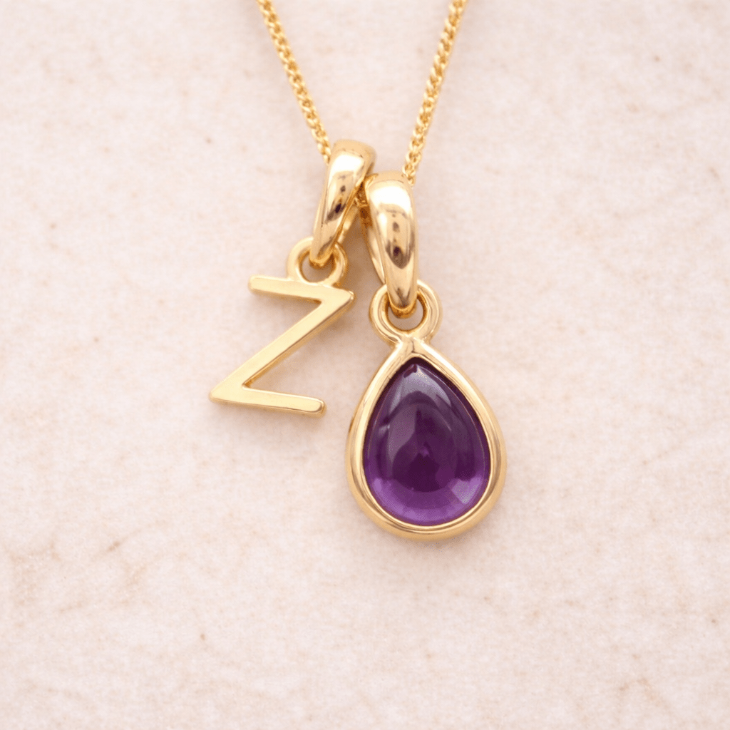 Gold necklace with a purple teardrop amethyst pendant and letter 'Z' charm on a beige background