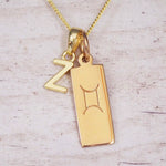 Gold initial Z and Gemini zodiac bar necklace, close-up of the letter charm and engraved pendant on whitewashed wood