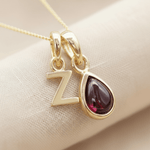 Gold necklace with 'Z' pendant and teardrop-shaped natural garnet gemstone on beige fabric background