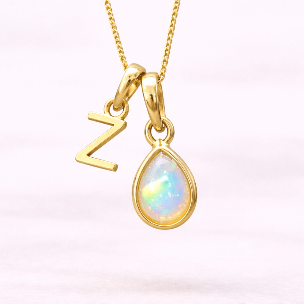 Gold necklace with 'Z' pendant and teardrop-shaped opal pendant on a light pink background