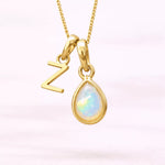 Gold October birthstone necklace with a pear-shaped natural opal pendant and letter 'Z' charm with a light background.