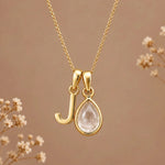 Gold initial J necklace with an April clear quartz teardrop on brown with dried flowers