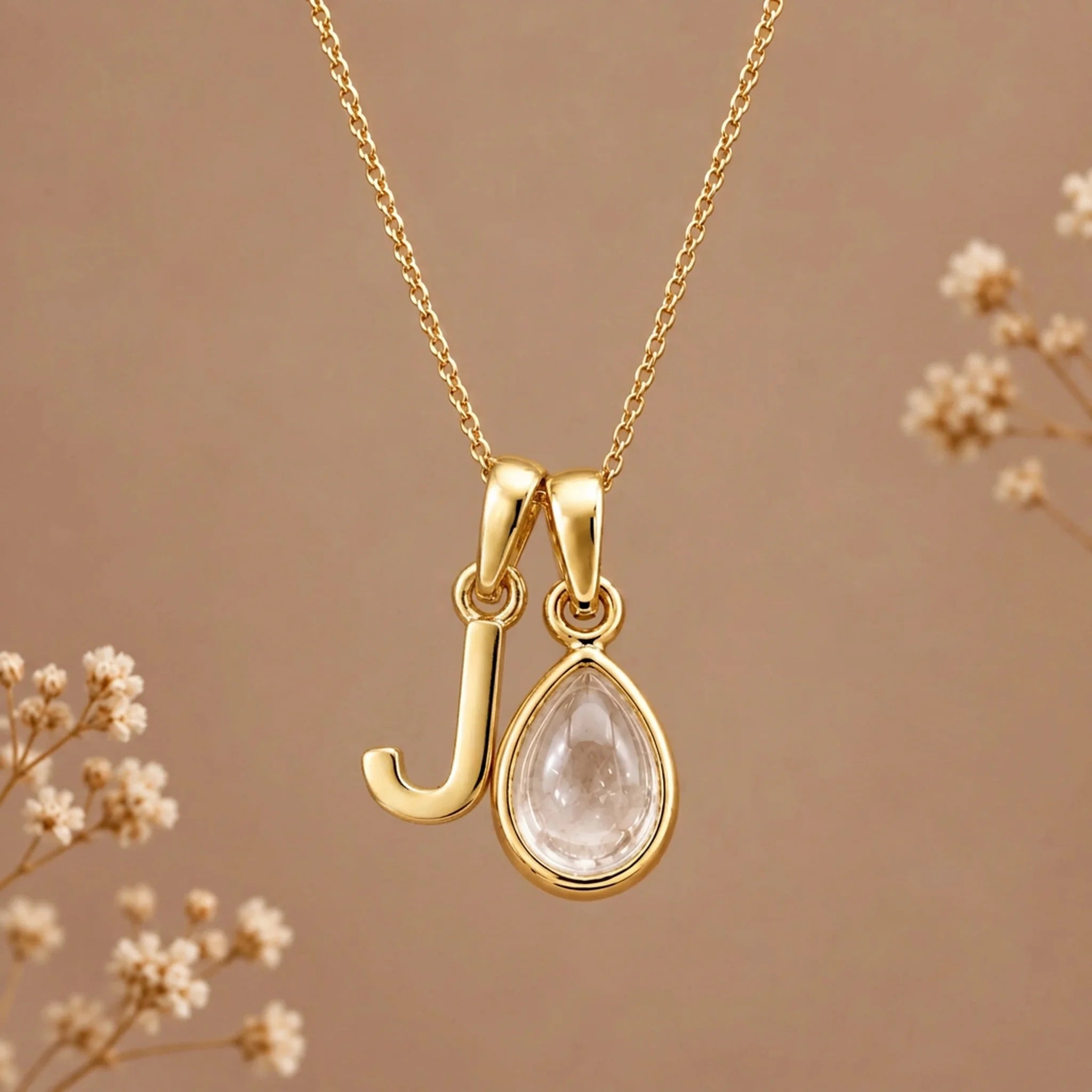 Gold initial J necklace with an April clear quartz teardrop on brown with dried flowers