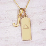 Gold initial and Libra zodiac necklace with a letter J charm and engraved bar pendant on whitewashed wood