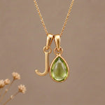 Gold Initial J Pendant and August birthstone Natural Peridot Necklace against a warm background