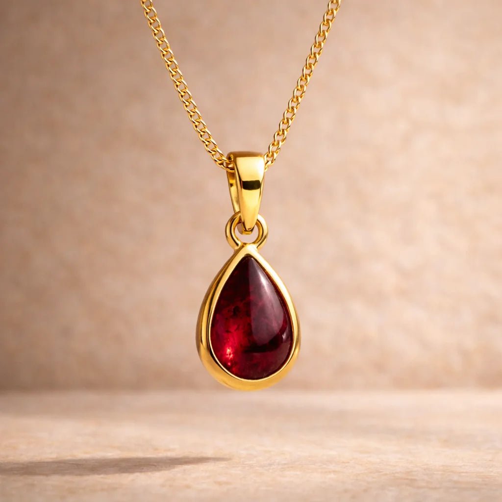 Gold necklace with a red teardrop natural garnet pendant on a beige background