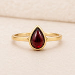 Gold ring with a red teardrop-shaped january birthstone natural garnet gemstone on a beige background