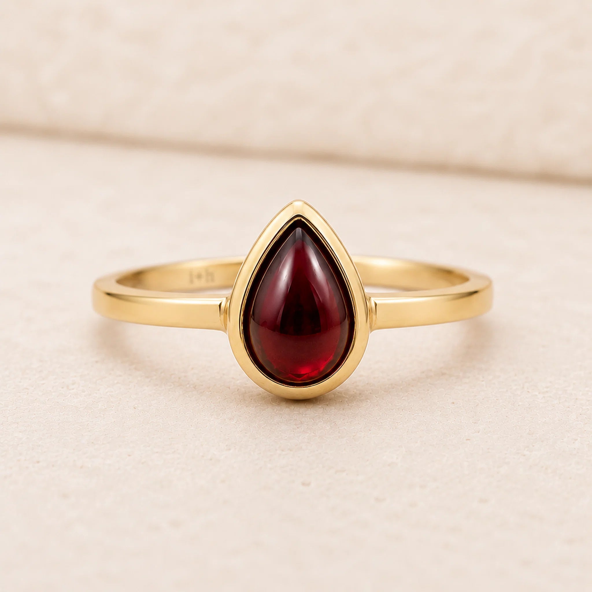 Gold ring with a red teardrop-shaped january birthstone natural garnet gemstone on a beige background
