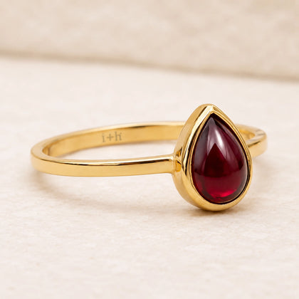 Gold ring with a red teardrop-shaped january birthstone natural garnet gemstone on a beige background