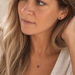 model wearing gold january birthstone jewellery set which includes dainty natural garnet pendant necklace and matching stud garnet earrings
