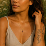 woman wearing a delicate gold january birthstone necklace with a natural garnet gemstone pendant against a blurred natural background