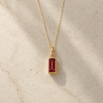 Gold fine chain necklace with a rectangle faceted bezel set january cubic zirconia pendant on a light stone background.