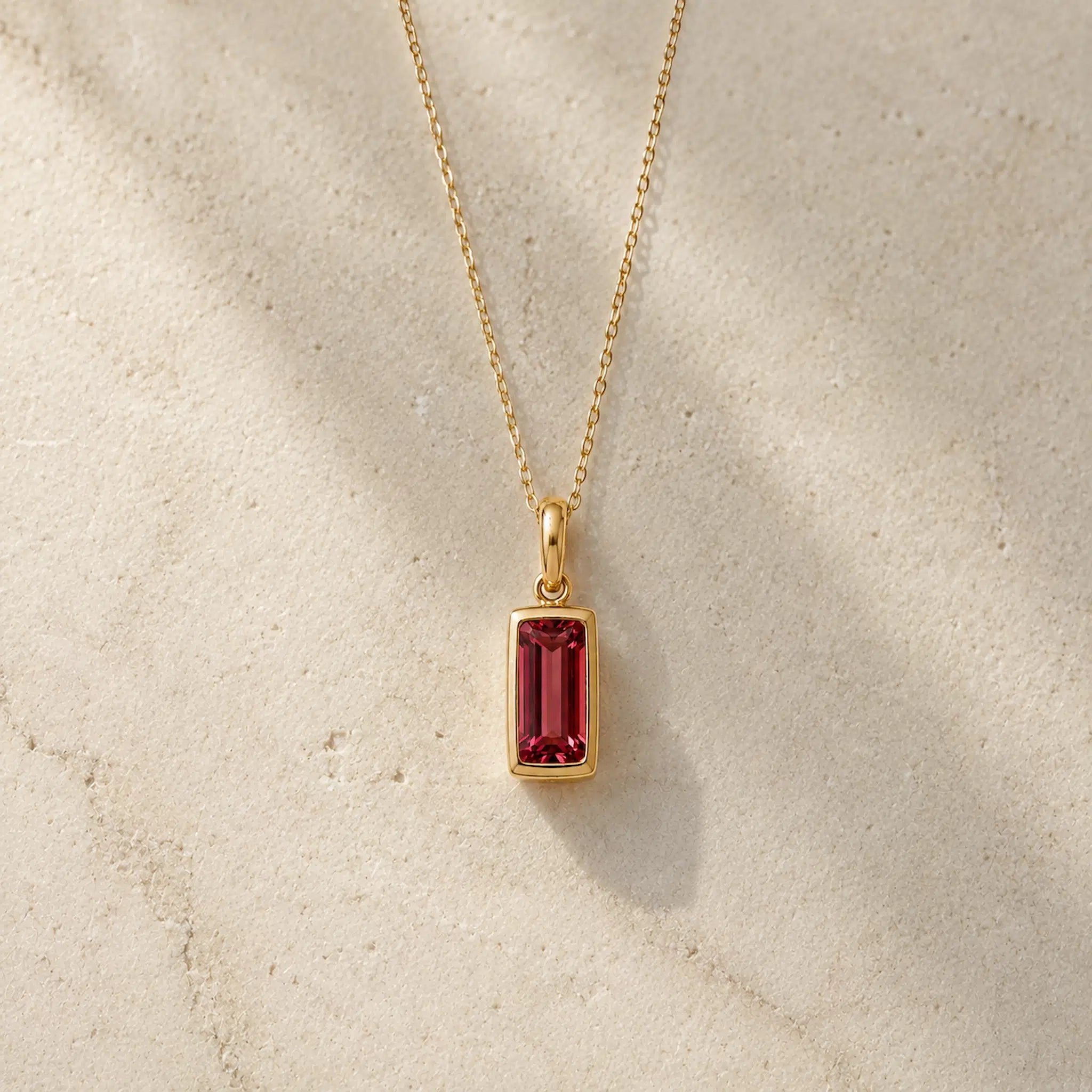 Gold fine chain necklace with a rectangle faceted bezel set january cubic zirconia pendant on a light stone background.