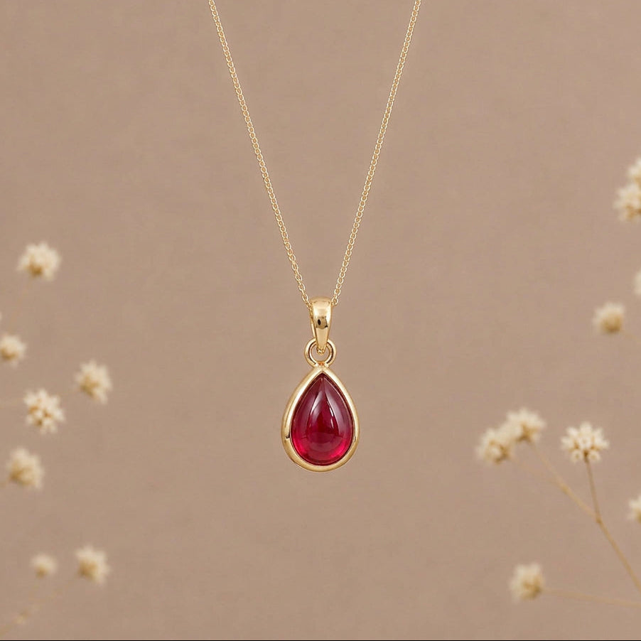 Gold July birthstone necklace with a teardrop ruby pendant, hanging