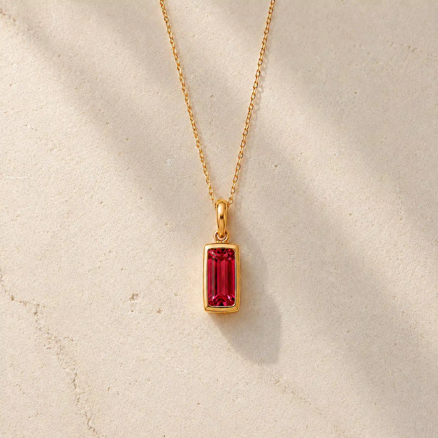 Gold fine chain necklace with a rectangle faceted bezel set july cubic zirconia pendant on a light stone background.