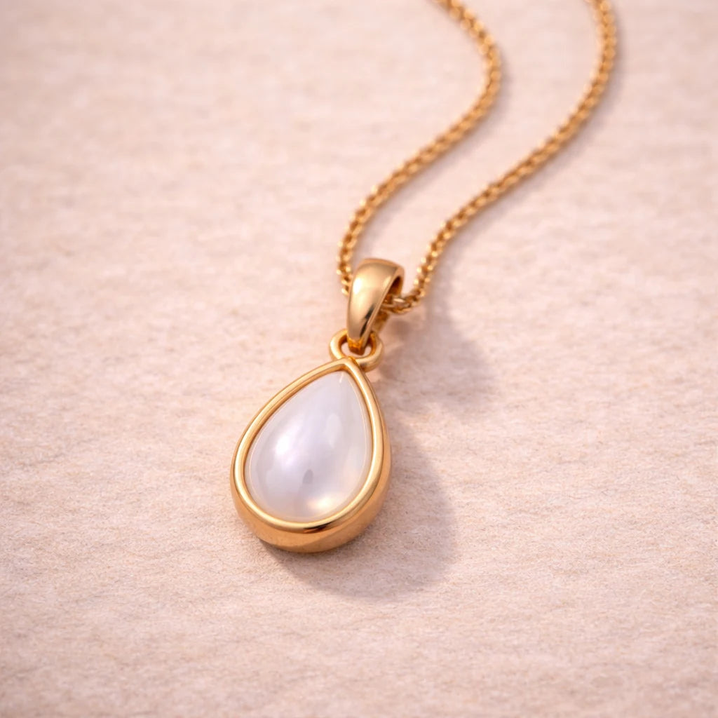 Gold necklace with a teardrop-shaped natural mother of pearl pendant on a soft pink background