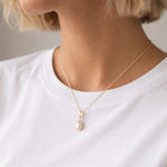 Gold necklace with a teardrop natural mother of pearl pendant worn by a person in a white shirt.