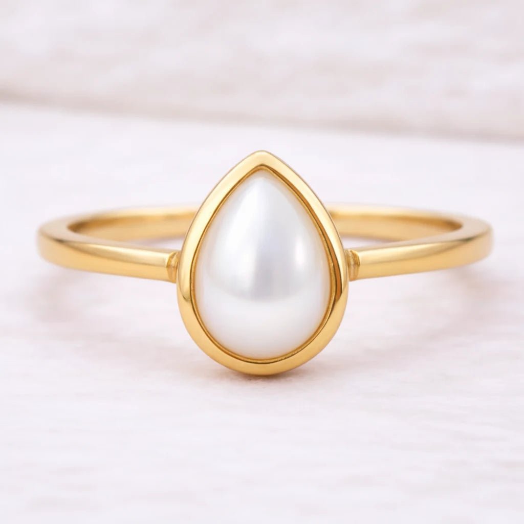 Gold ring with a teardrop-shaped pearl on a light background