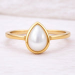Gold ring with a teardrop-shaped pearl on a light background