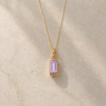 Gold fine chain necklace with a rectangle faceted bezel set june cubic zirconia pendant on a light stone background.