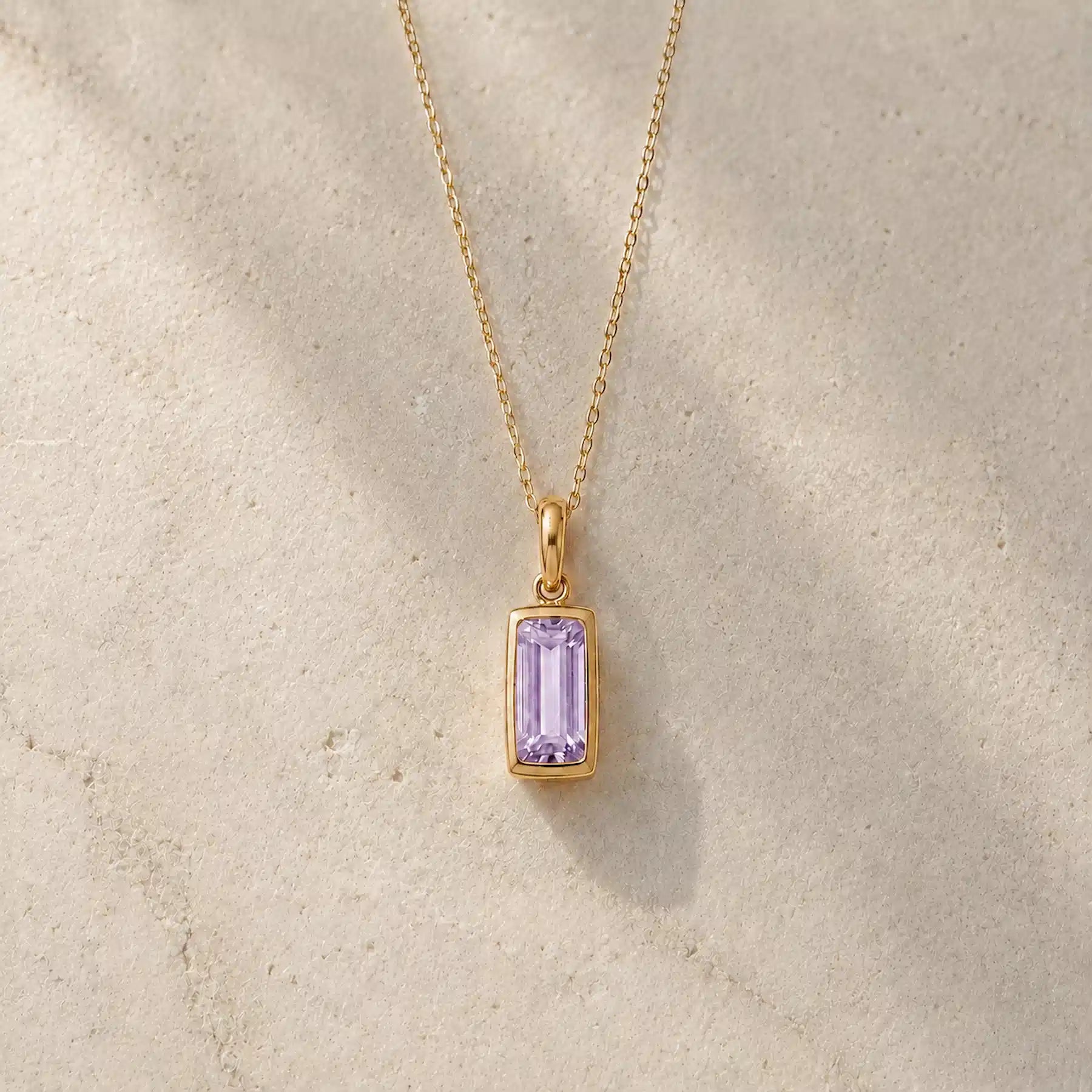Gold fine chain necklace with a rectangle faceted bezel set june cubic zirconia pendant on a light stone background.