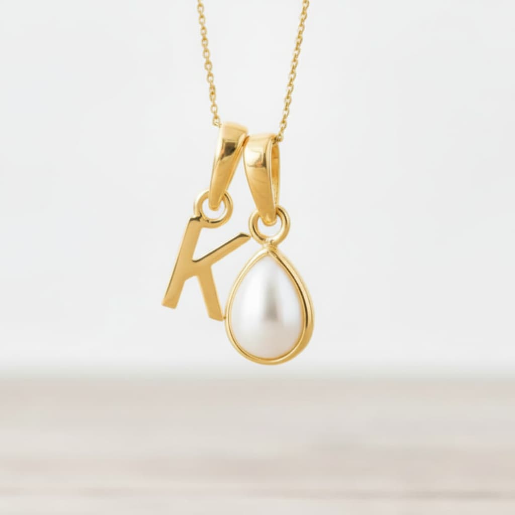 Gold necklace with 'K' pendant and pearl on a light background