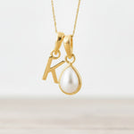Gold necklace with 'K' pendant and pearl on a light background