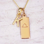 Gold initial and Libra zodiac necklace with a letter K charm and engraved bar pendant on whitewashed wood