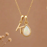 Gold Initial K Pendant and October birthstone Natural Opal Necklace against a warm background