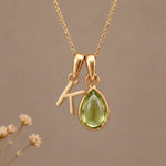 Gold Initial K Pendant and August birthstone Natural Peridot Necklace against a warm background
