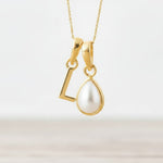 Gold initial L necklace with a teardrop-shaped pearl pendant on a light background