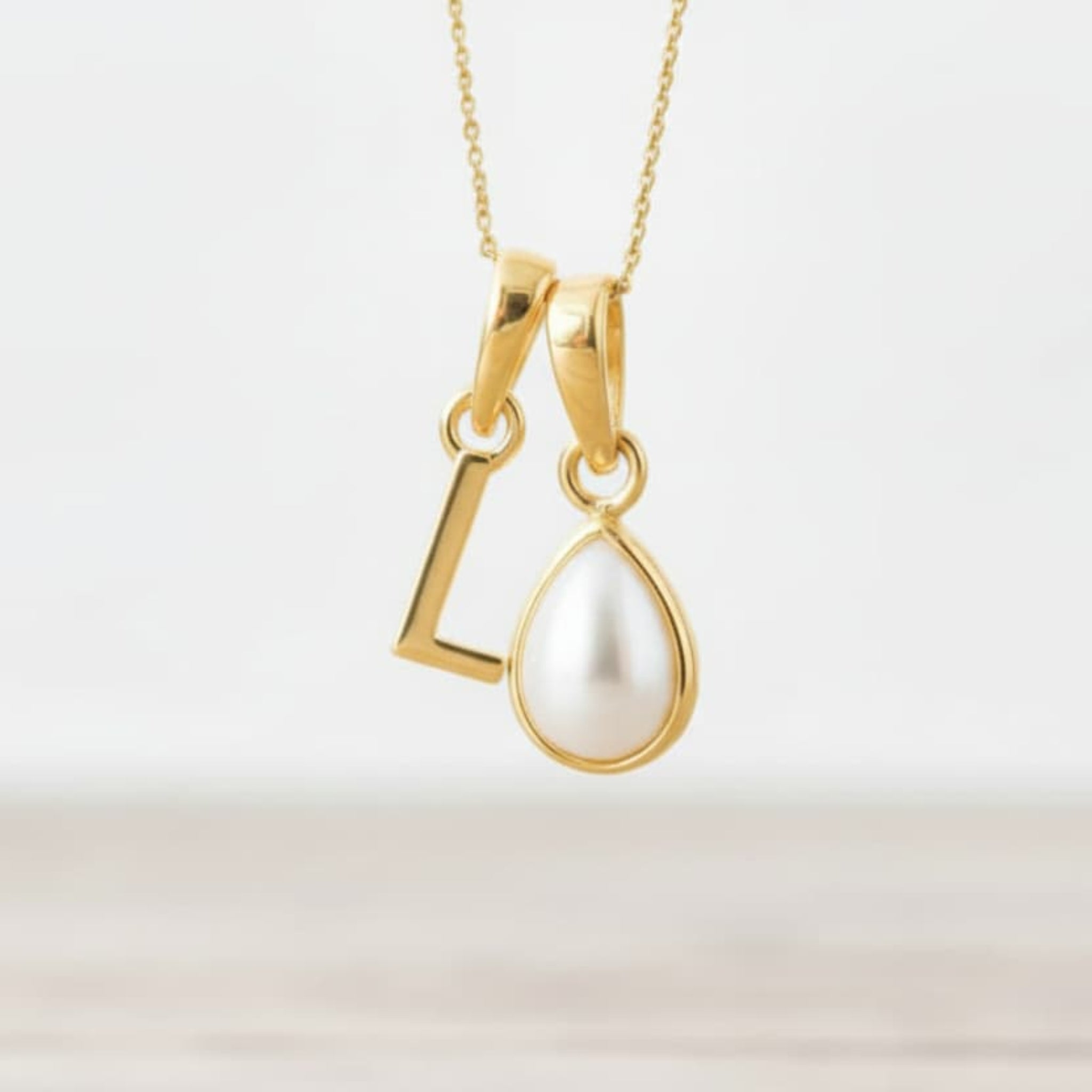 Gold June birthstone necklace with a pear-shaped natural mother of pearl pendant and letter 'L' charm.