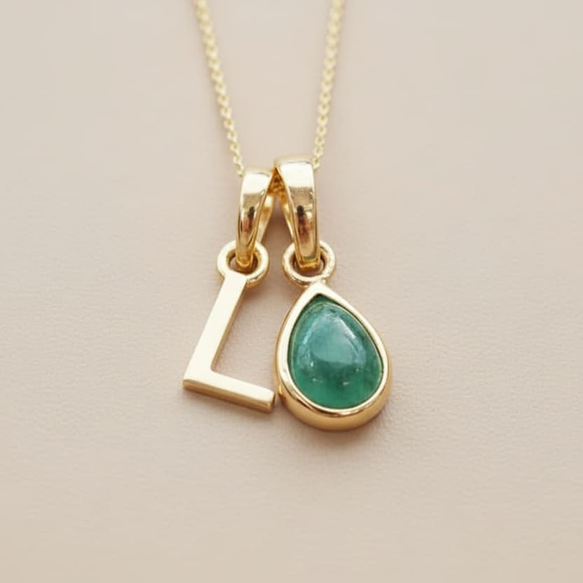 Gold necklace with a green teardrop pendant on a beige background