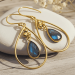 Gold earrings with blue teardrop stones on a stone surface