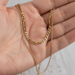 Gold double chain necklace held in a hand against a neutral background
