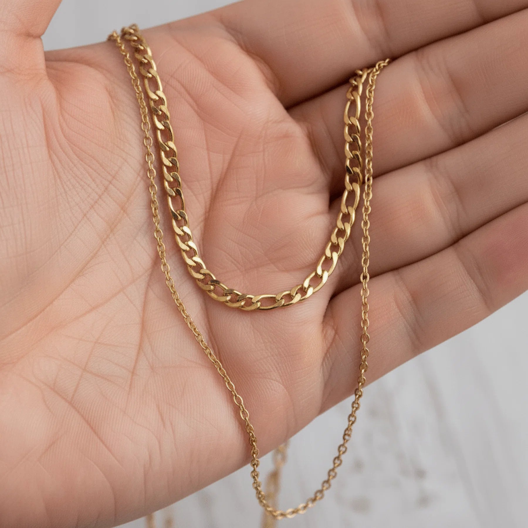 Gold double chain necklace held in a hand against a neutral background