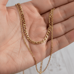 Gold chain necklace held in a hand against a neutral background