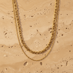 Gold chain necklace on a beige stone surface