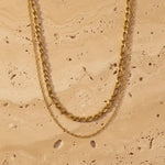 Gold double chain necklace on a beige stone surface