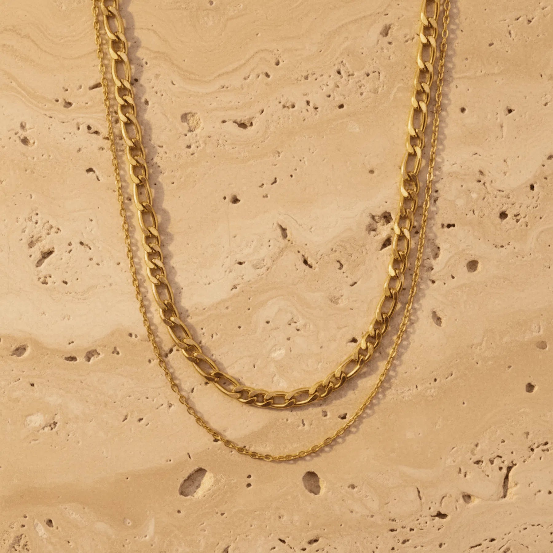 Gold double chain necklace on a beige stone surface