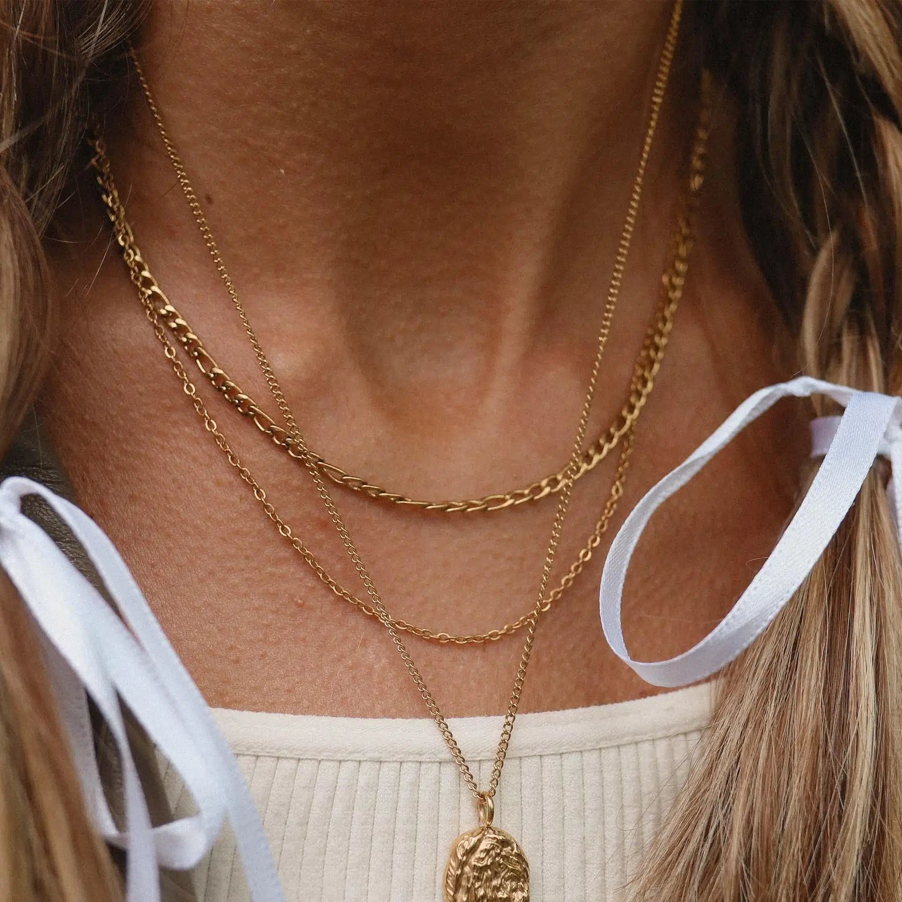 Close-up of a person wearing gold layered chain necklace 