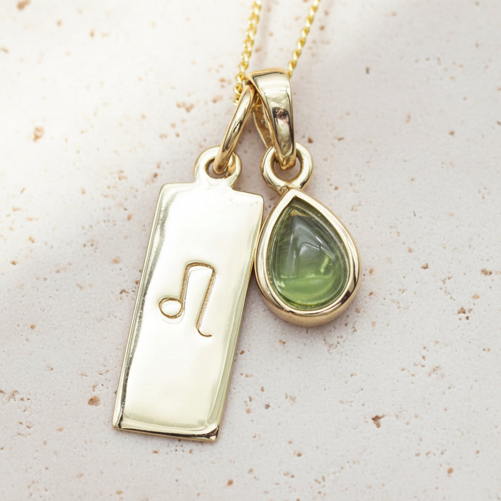 Gold necklace with a green teardrop natural peridot pendant and a rectangular leo zodiac pendant on a textured surface