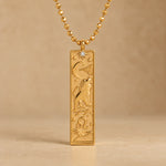 Gold Leo zodiac necklace, embossed bar pendant with sign symbol on a faceted ball chain, warm beige background