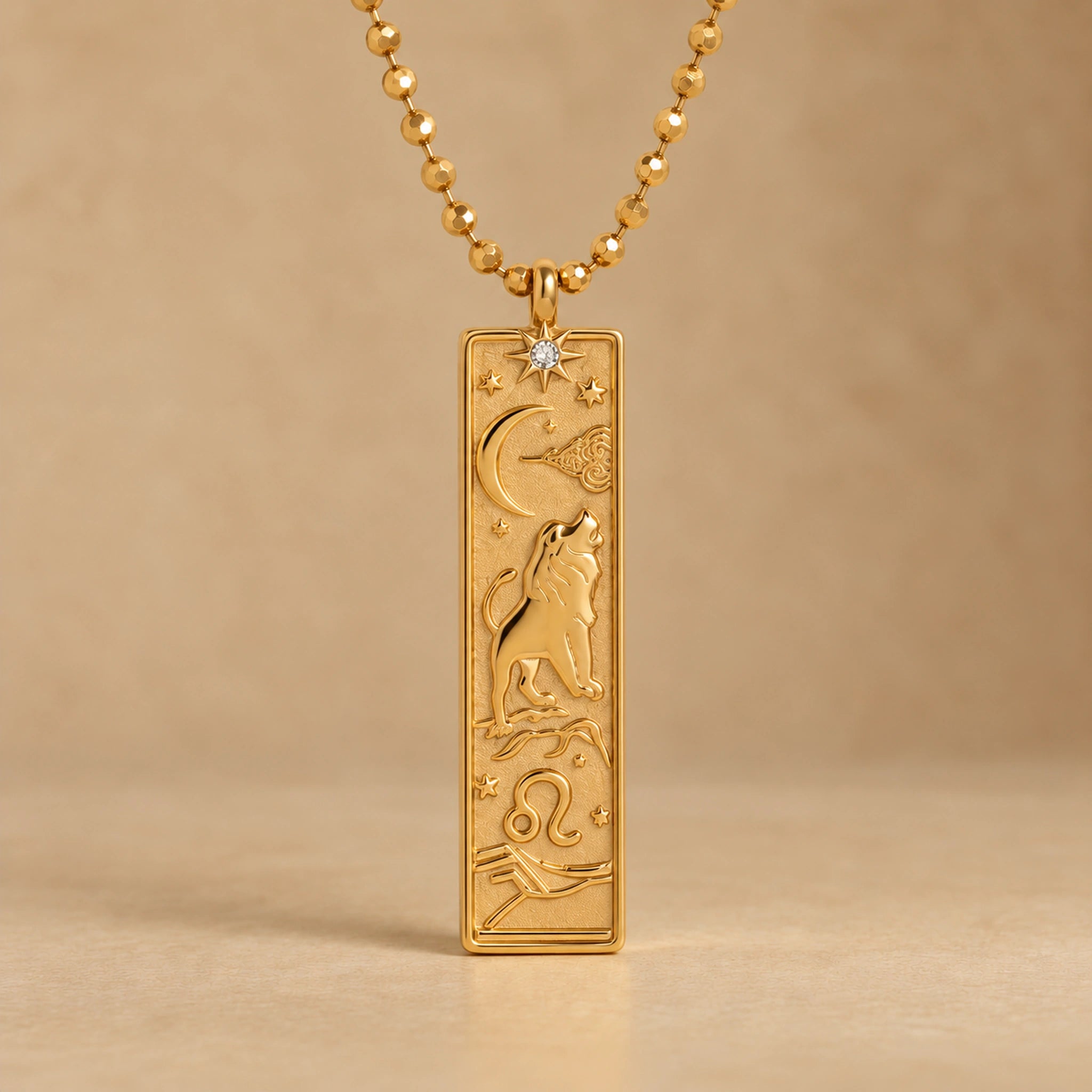 Gold Leo zodiac necklace, embossed bar pendant with sign symbol on a faceted ball chain, warm beige background