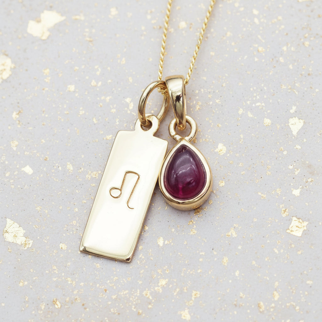 Gold necklace with a Leo Zodiac symbol pendant and a tear drop red ruby gemstone on a natural background