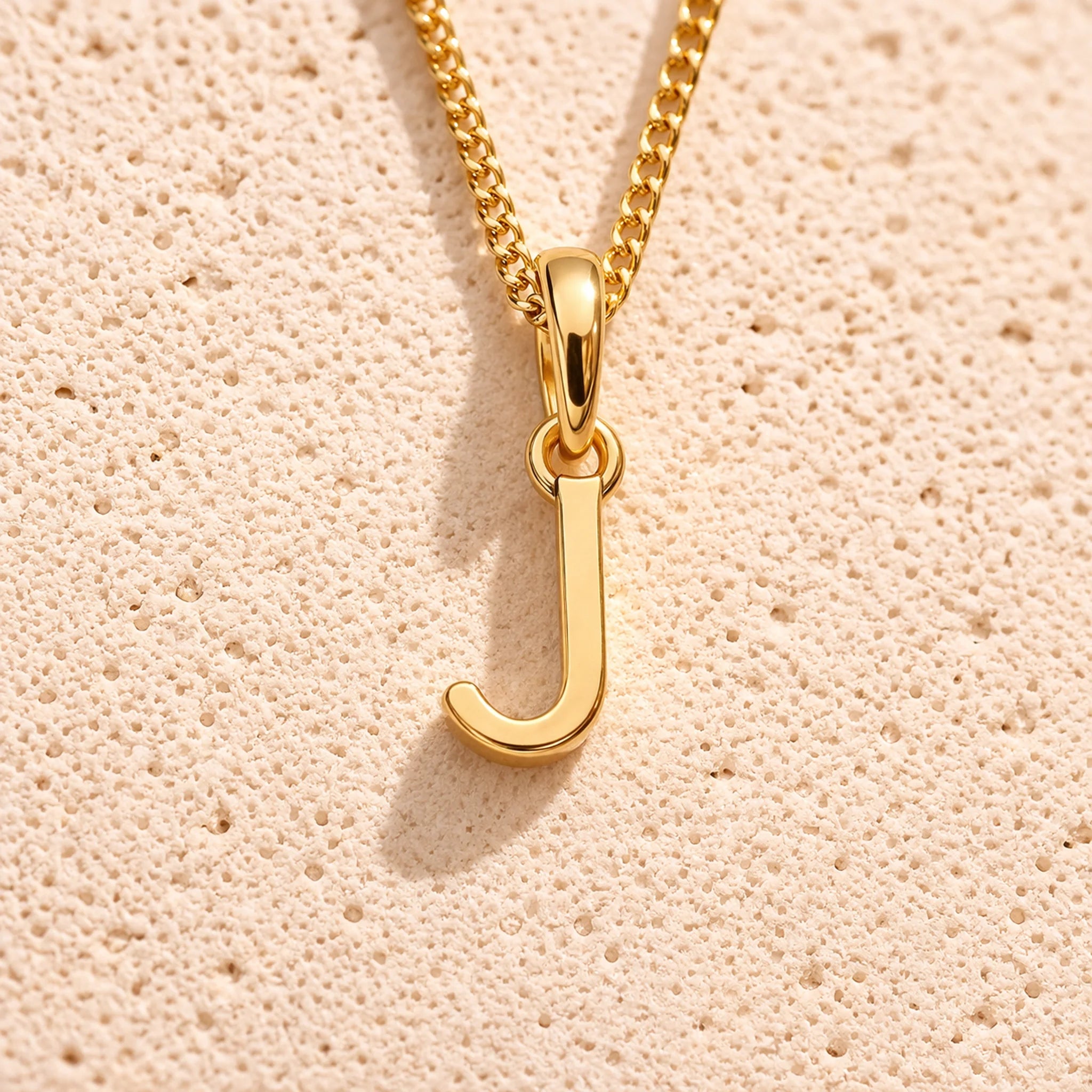 Personalised Gold initial necklace with a minimalist ‘J’ initial pendant on a light stone background