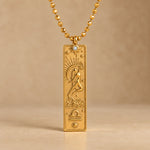 Gold Libra zodiac necklace, embossed bar pendant with sign symbol on a faceted ball chain, warm beige background