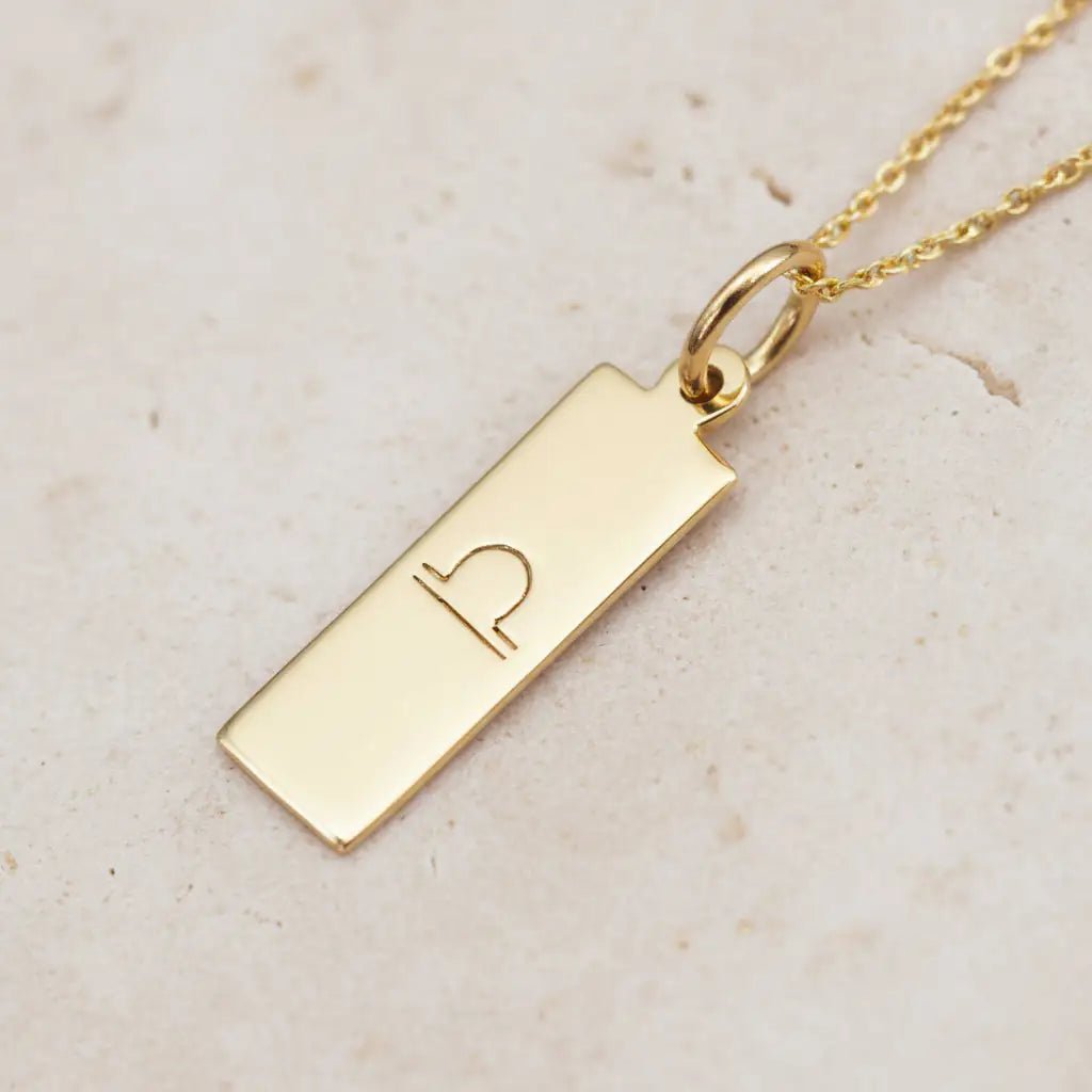 gold libra zodiac pendant necklace on a light stone surface
