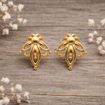 Gold lotus stud earrings on a wooden surface with small white flowers